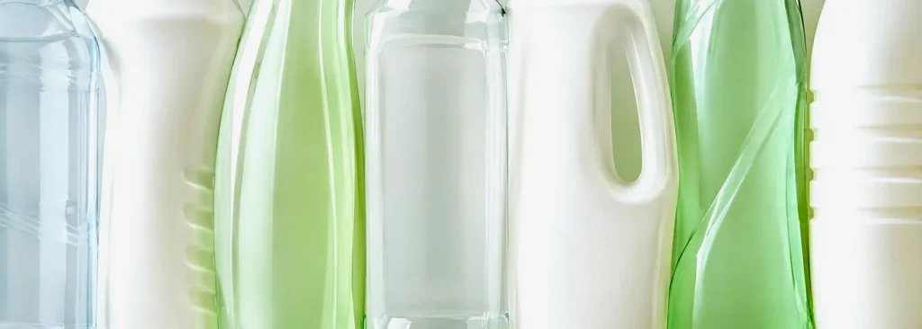 Row of unbranded household cleaning bottles in pale blue, white and green plastic, the packaging formats covered by PPWR recyclability rules