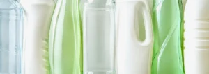 Row of unbranded household cleaning bottles in pale blue, white and green plastic, the packaging formats covered by PPWR recyclability rules