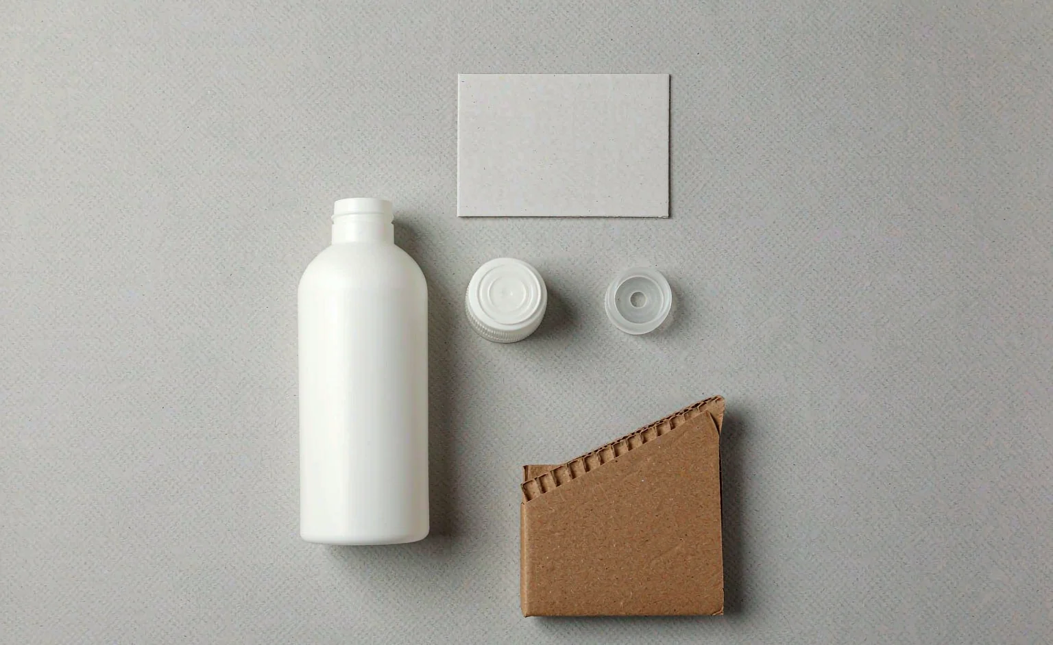 Household cleaning product packaging components laid out for weighing: a bottle, a cap, a label and a carton